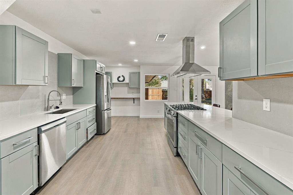 Kitchen featuring stainless steel appliances, light-toned shaker cabinetry, stone-surface countertops, a stainless steel range hood, and wood-finish flooring
