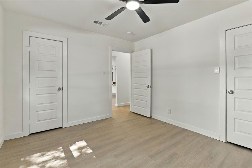 Neutral-toned wood-finish flooring, crisp white walls, and matte black ceiling-mounted light fixture with a five-blade fan