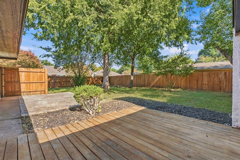 Backyard featuring a wood deck, concrete patio, perimeter wood fencing, and mature trees