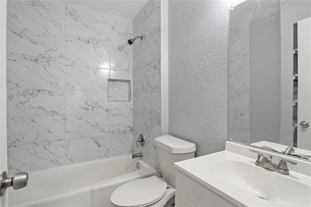 Full-height shower surround with veined tile finish and built-in recessed niche, chrome shower hardware, vanity cabinet with integrated sink basin, chrome dual-handle faucet, and frameless wall-mounted mirror