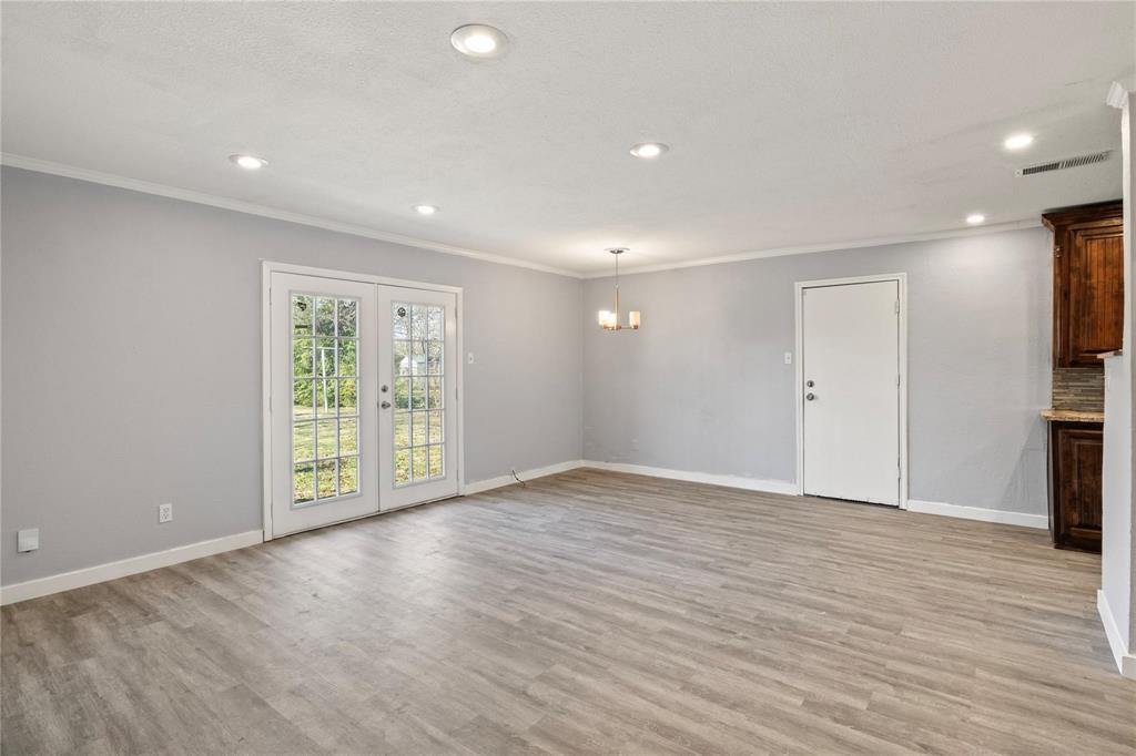 Neutral-toned interior space featuring wood-finish flooring, recessed lighting, double French doors, and a multi-light chandelier