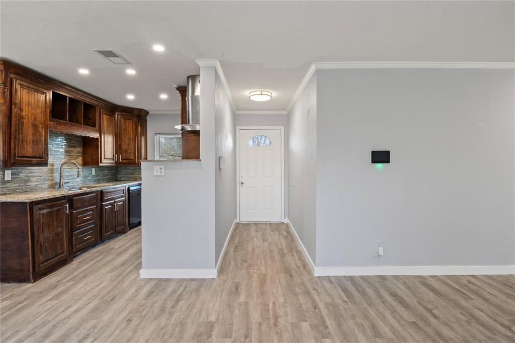 Kitchen featuring wood-finish cabinetry, stone-texture backsplash, and stone-look countertops, accompanied by wood-finish flooring and a single-light entry door