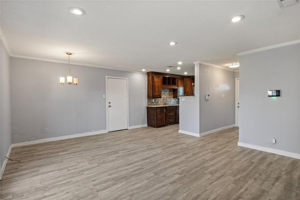 Living area featuring wood-finish flooring, recessed lighting, and a multi-light chandelier, with a partial wall revealing kitchen cabinetry and a tiled backsplash