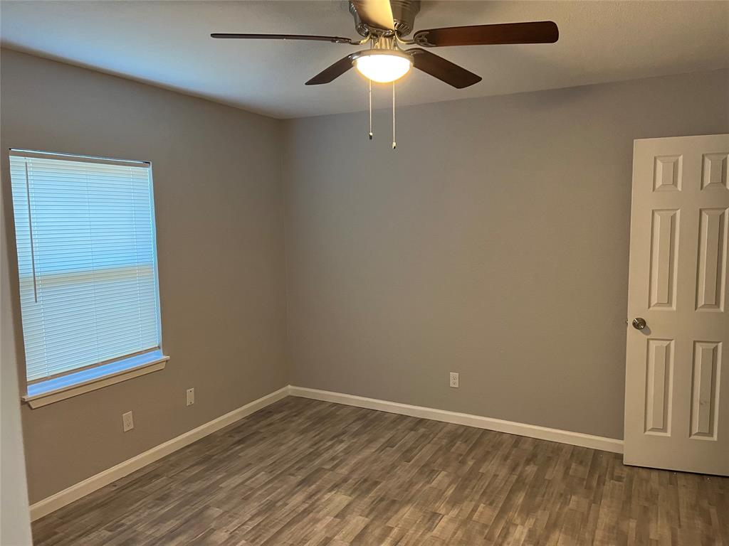 Room featuring neutral wall paint, wood-finish flooring, a six-panel interior door, and a ceiling fan with integrated lighting