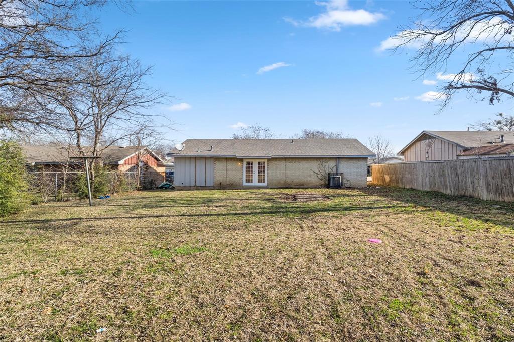 Backyard featuring a brick exterior, French doors, wood-plank fencing, and mature trees