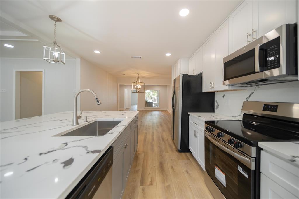 Kitchen featuring an expansive island with a waterfall edge, quartz countertops, white shaker-style cabinetry, stainless steel appliances, and wood-finish flooring