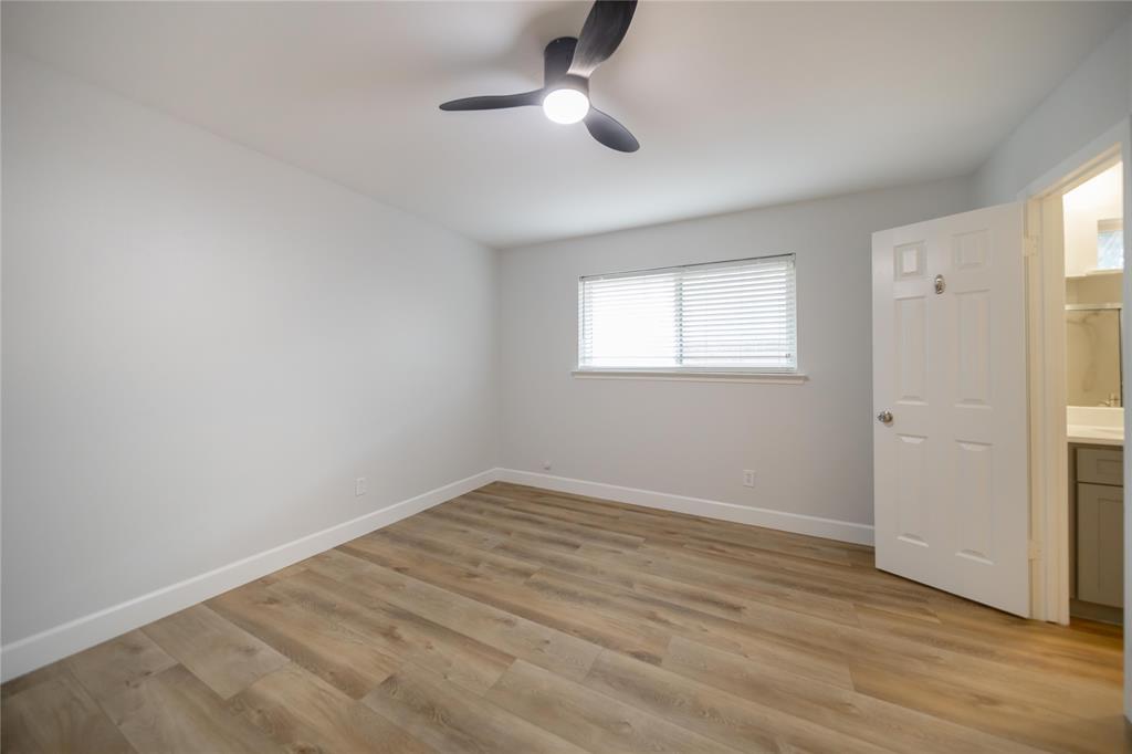 Neutral interior room featuring wood-finish flooring, a modern multi-blade ceiling fan with integrated lighting, and a window with fitted horizontal blinds