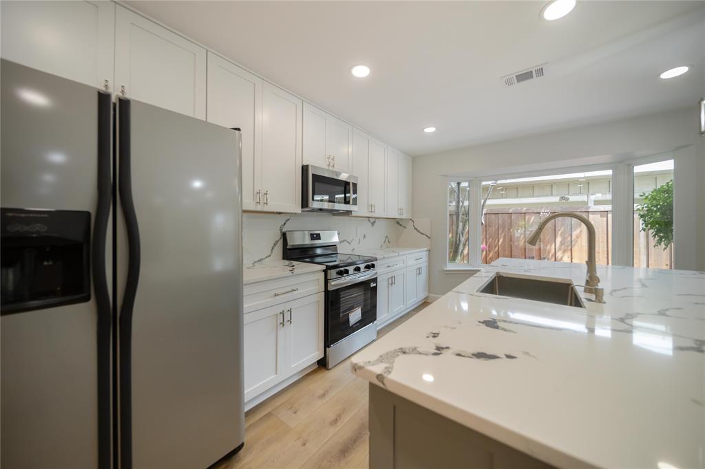 Kitchen featuring white Shaker-style cabinetry, quartz countertops with veining, wood-finish flooring, stainless steel appliances, and a central island with an undermount sink Kitchen featuring white Shaker-style cabinetry, quartz countertops with veining, wood-finish flooring, stainless steel appliances, and a central island with an undermount sink