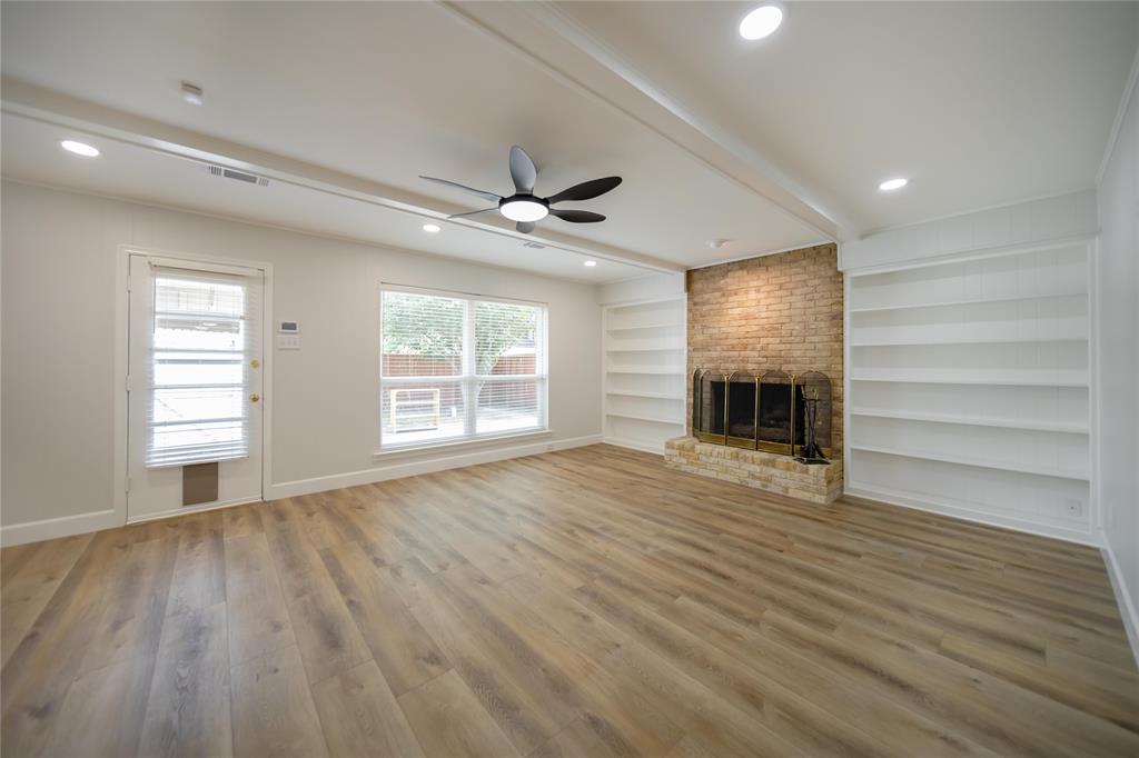 Living area featuring wood-finish flooring, a masonry fireplace with a stone hearth, built-in shelving, a ceiling fan, and recessed lighting