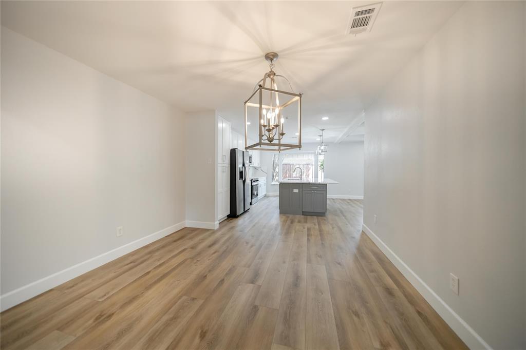 Open-concept area featuring wood-finish flooring, a geometric metal-frame chandelier, and a central kitchen island with cabinetry Open-concept area featuring wood-finish flooring, a geometric metal-frame chandelier, and a central kitchen island with cabinetry