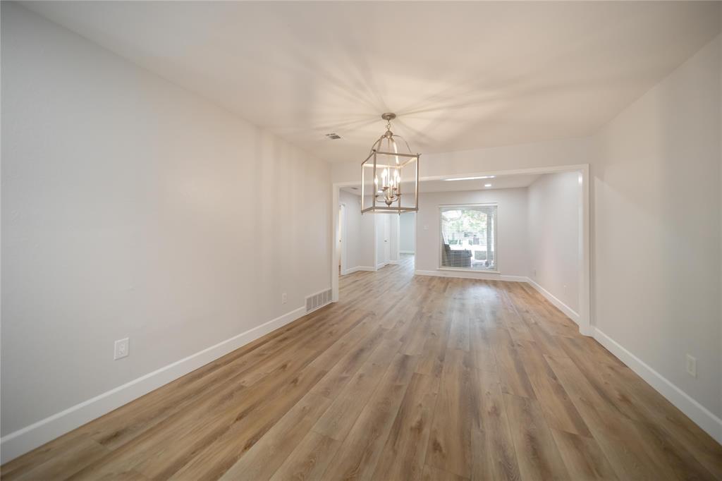 Open-concept interior featuring wood-finish flooring, neutral wall paint, and a decorative lantern-style metal pendant light Open-concept interior featuring wood-finish flooring, neutral wall paint, and a decorative lantern-style metal pendant light