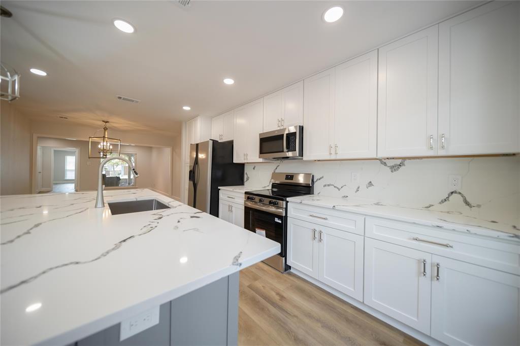 Kitchen featuring white shaker cabinetry, stone-patterned countertops, a coordinating full-height backsplash, stainless steel appliances, and a central island with a built-in sink