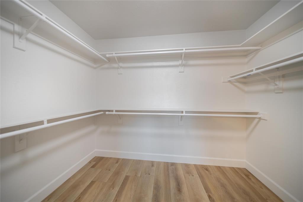 Walk-in storage space featuring wood-finish flooring, white walls, and tiered wall-mounted shelving with integrated hanging rods