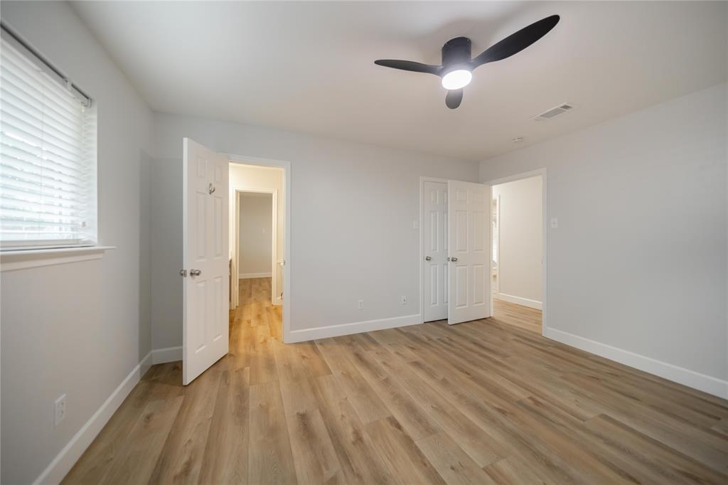 Neutral-toned interior featuring wood-finish flooring, a modern three-blade ceiling fan with integrated lighting, and horizontal slatted window blinds