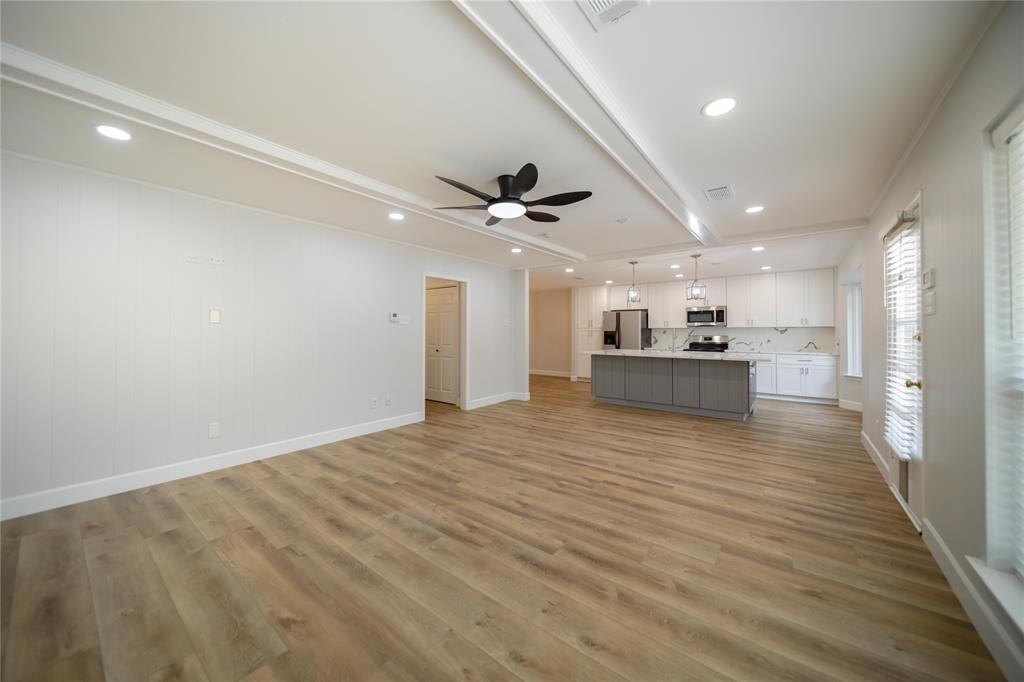 Open-concept interior featuring wood-finish flooring, tray ceiling with recessed lighting, kitchen island with stone-finish countertop, white shaker-style cabinetry, and matte black ceiling fan
