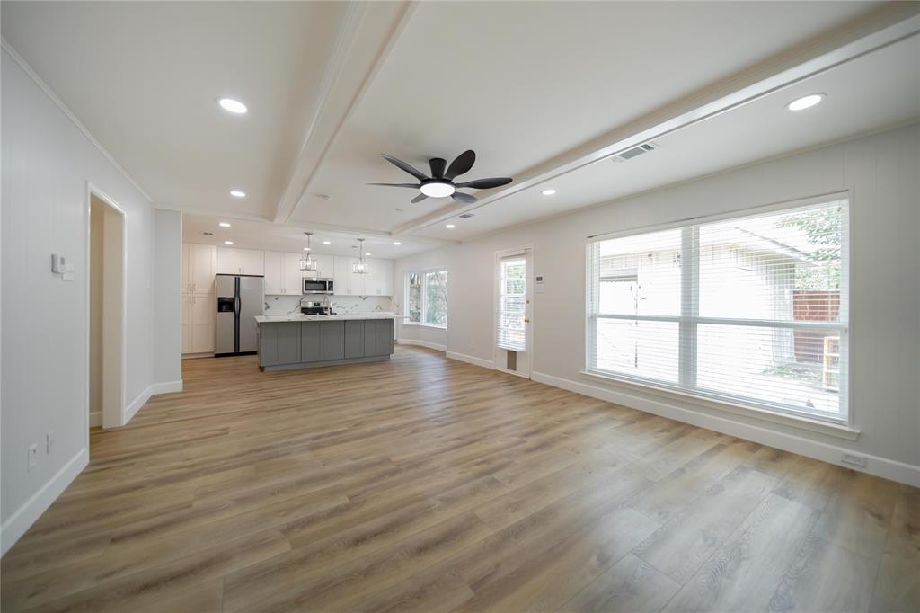 Open-concept space featuring wood-finish flooring, recessed lighting, a center island with contrasting cabinetry, and large windows with horizontal blinds