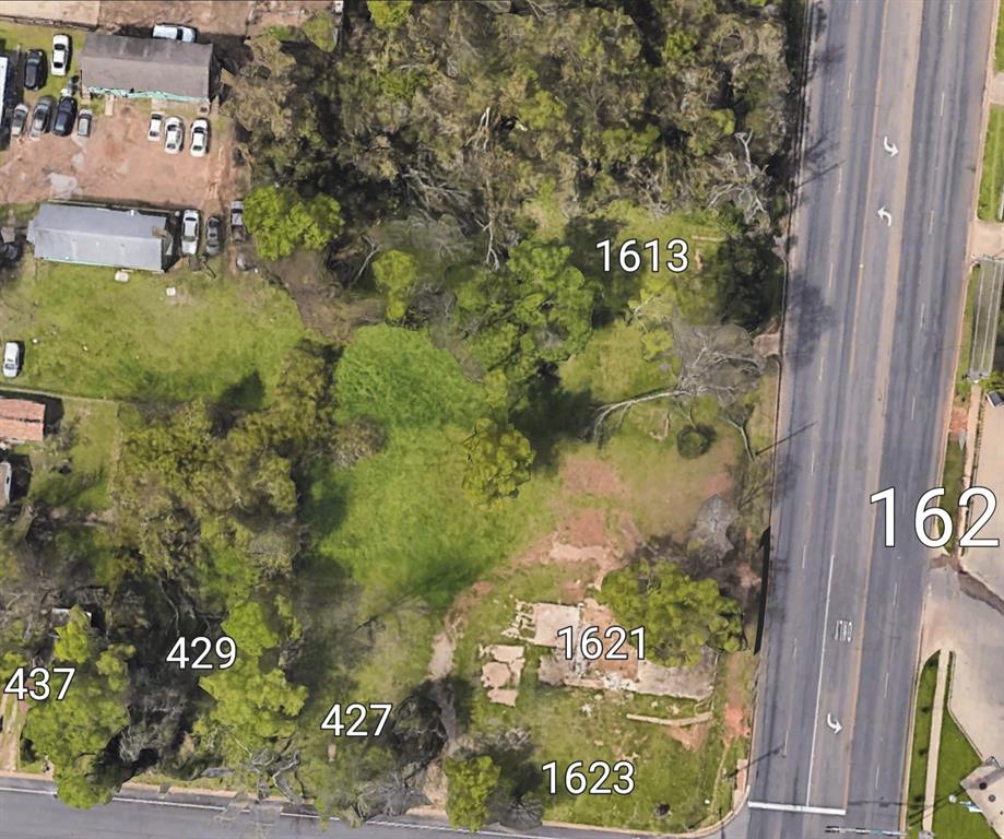 Expansive corner parcel featuring mature trees, established grass cover, and direct access to a paved thoroughfare