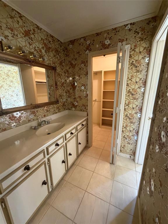 Vanity featuring a solid-surface countertop with an integrated basin, white cabinetry, ceramic tile flooring, and a walk-in storage area with built-in shelving