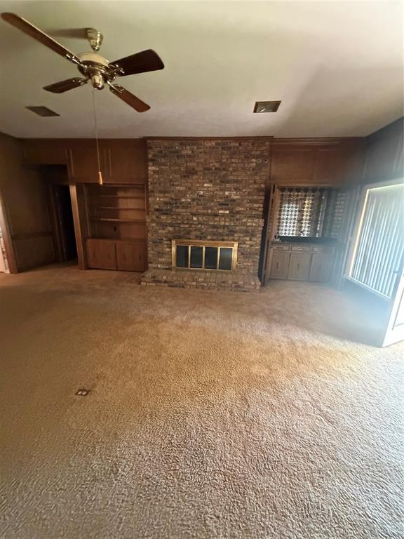 Floor-to-ceiling brick fireplace with a metal insert, built-in wood cabinetry, and a ceiling fan Floor-to-ceiling brick fireplace with a metal insert, built-in wood cabinetry, and a ceiling fan
