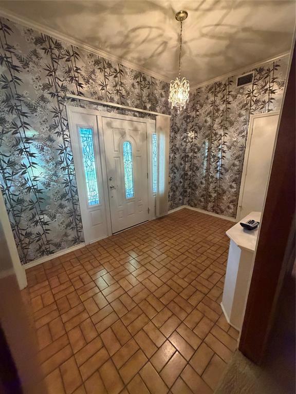 Entryway featuring patterned wallpaper, ceramic tile flooring in a herringbone pattern, a crystal-style multi-arm pendant light, and a white entry door with decorative glass inserts Entryway featuring patterned wallpaper, ceramic tile flooring in a herringbone pattern, a crystal-style multi-arm pendant light, and a white entry door with decorative glass inserts