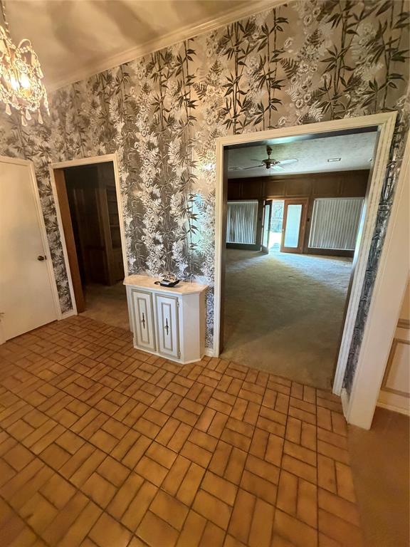 Foyer featuring patterned wall coverings, brick-style flooring, a crystal-style chandelier, and a built-in cabinet with a stone-top surface Foyer featuring patterned wall coverings, brick-style flooring, a crystal-style chandelier, and a built-in cabinet with a stone-top surface