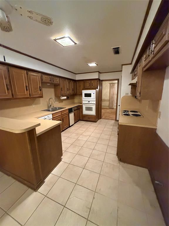 Kitchen featuring wood cabinetry, tile flooring, built-in double wall oven, integrated cooktop, and peninsula counter space Kitchen featuring wood cabinetry, tile flooring, built-in double wall oven, integrated cooktop, and peninsula counter space
