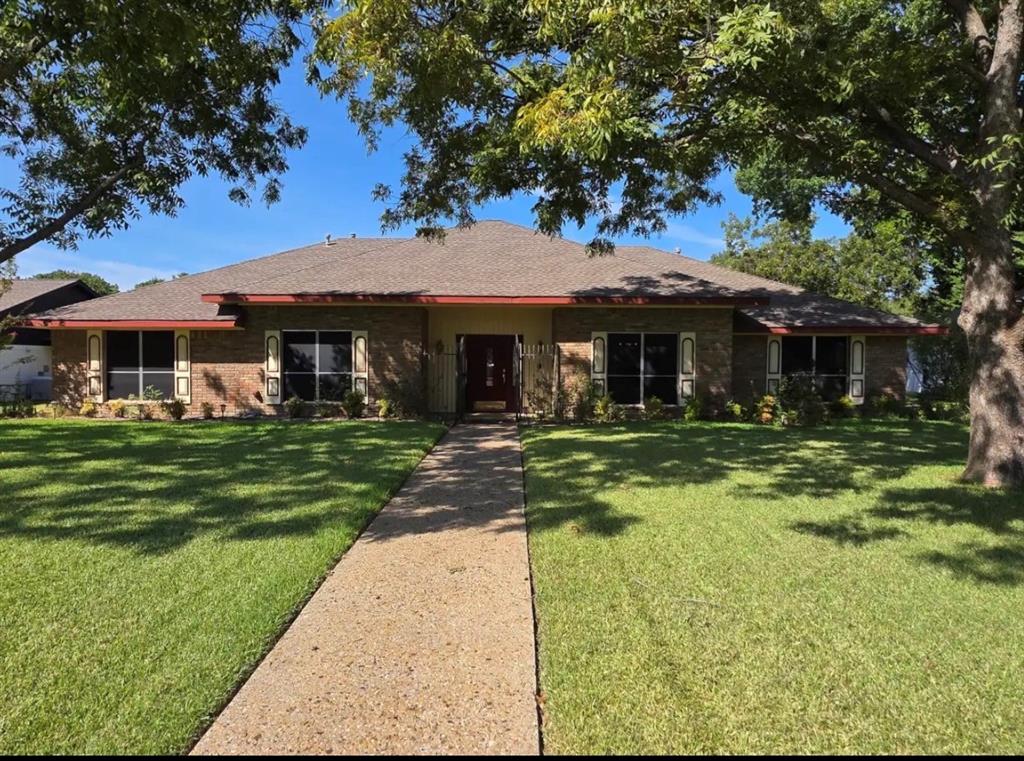 Single-story brick exterior featuring a hip roof, central entryway with detailed front door, rectangular window shutters, and a concrete walkway