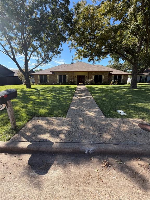 Single-story brick exterior featuring a hip roof, concrete walkway, and mature trees Single-story brick exterior featuring a hip roof, concrete walkway, and mature trees