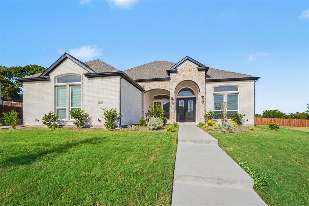 Single-story exterior featuring light-toned brick and stone veneer, arched covered entryway, double-door front entrance, and arched windows