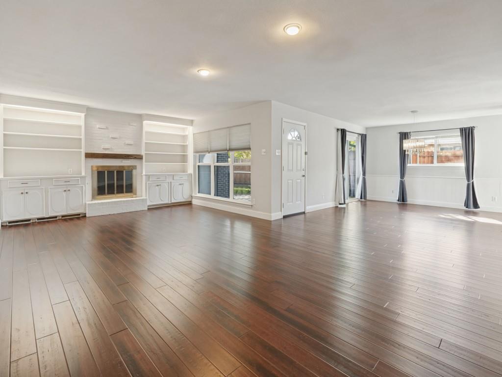 Open-concept room featuring wood-finish flooring, a fireplace with a wood mantel, built-in shelving and cabinetry, recessed lighting, and wall-panel molding