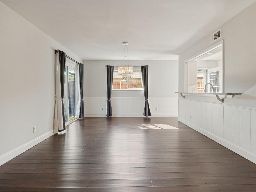 Interior featuring dark wood-finish flooring, white wainscoting, a tiered crystal chandelier, and a pass-through opening with an extended stone ledge