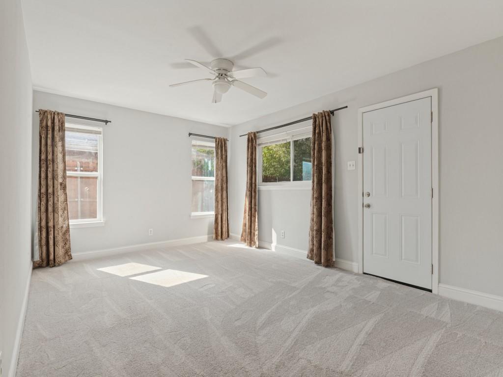Neutral-toned interior space featuring light-colored wall-to-wall carpeting, three windows with natural light exposure, and a ceiling-mounted fan