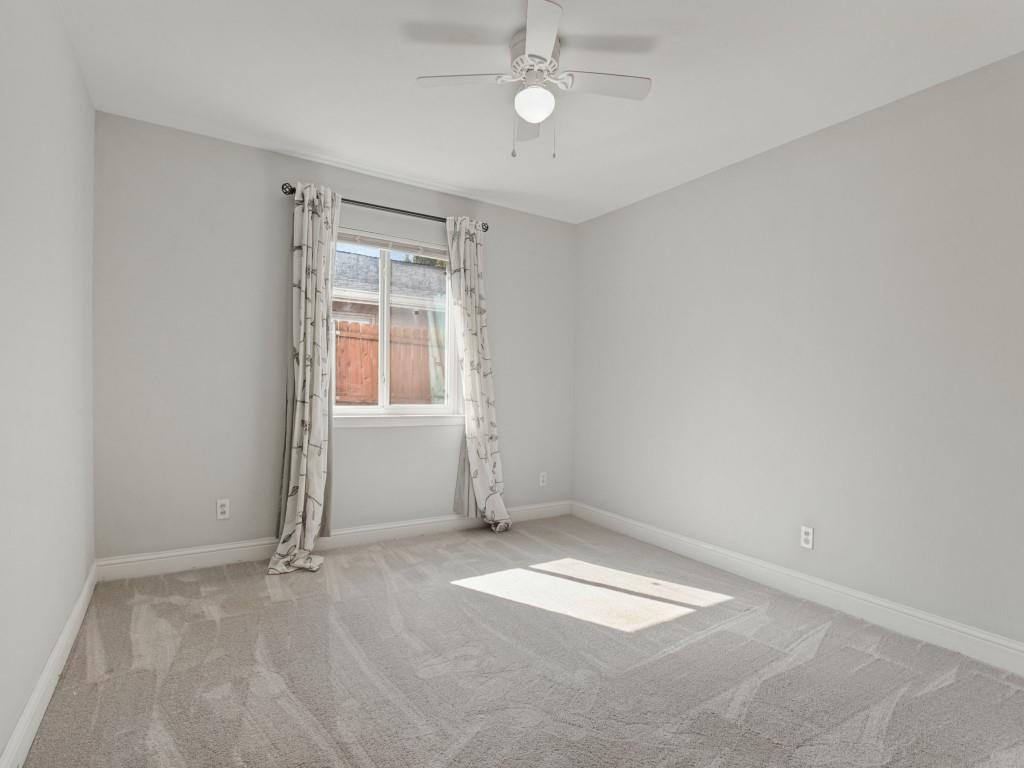Neutral interior space featuring wall-to-wall carpeting, a multi-blade ceiling fan with integrated lighting, and a single-pane window with a curtain rod