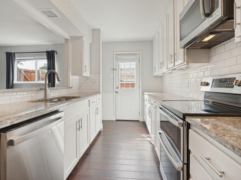 Kitchen featuring white cabinetry, stone-finish countertops, subway tile backsplash, stainless steel appliances, and wood-finish flooring
