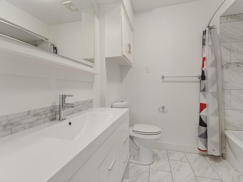 Bathroom featuring a white vanity with an integrated sink, polished chrome faucet, stone-tile backsplash, and tile flooring arranged in a herringbone pattern
