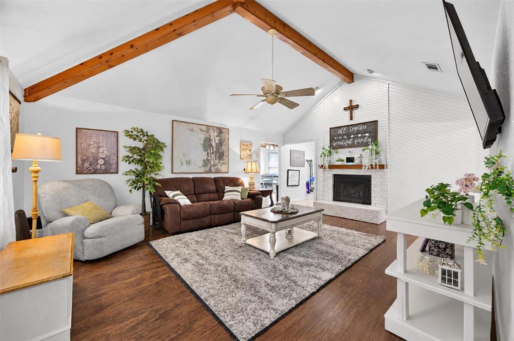 Vaulted ceiling featuring exposed wood beams, wood-finish flooring, and a floor-to-ceiling painted brick fireplace with a wood mantel