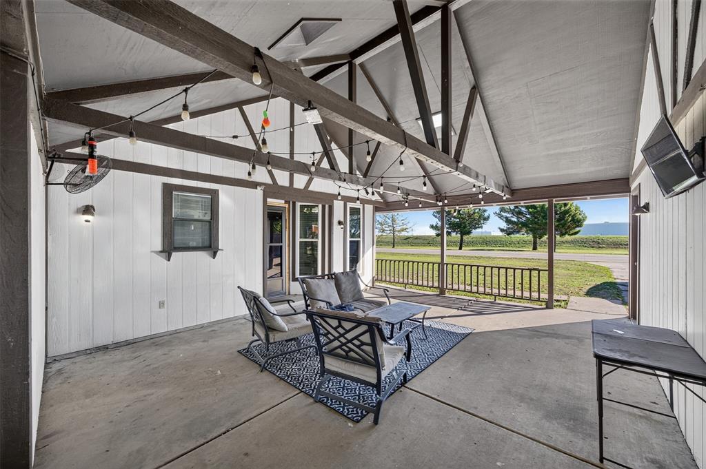 Covered patio featuring a vaulted ceiling with exposed timber trusses, concrete flooring, and an attached wood railing overlooking open grounds