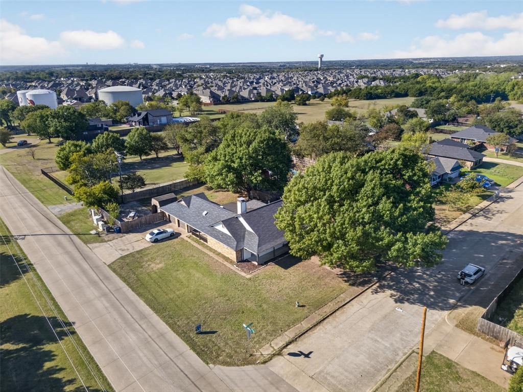 Aerial perspective of a corner lot property featuring a multi-gabled asphalt shingle roof, masonry exterior, and mature tree canopy