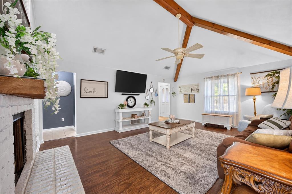 Vaulted ceilings featuring exposed timber beams, wood-finish flooring, and a floor-to-ceiling painted brick fireplace