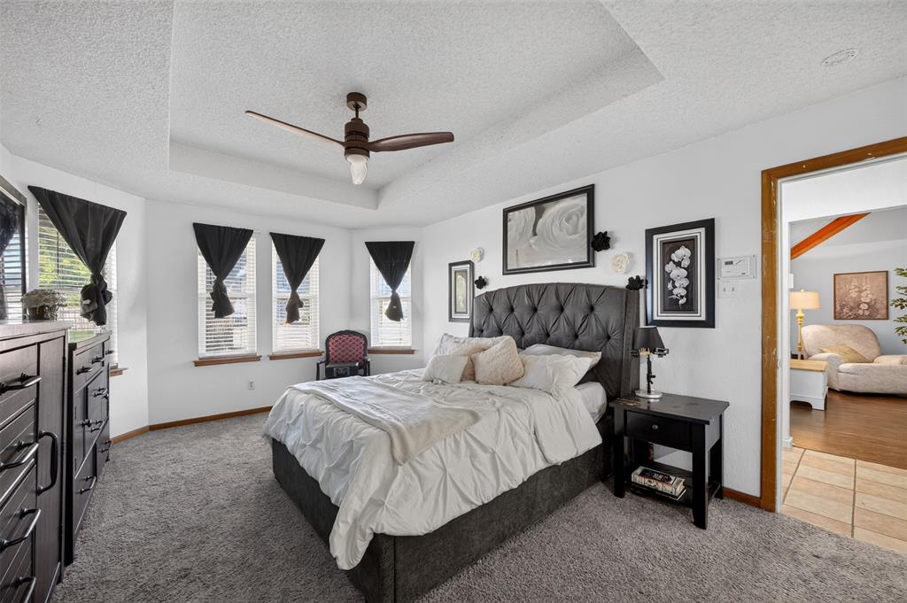 Tray ceiling featuring a central multi-blade ceiling fan, expansive triple-pane bay windows, and neutral carpeting