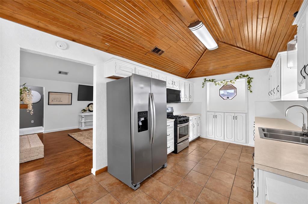 Kitchen featuring vaulted wood-plank ceilings, tile flooring, white cabinetry, a built-in recessed display niche, and stainless steel appliances