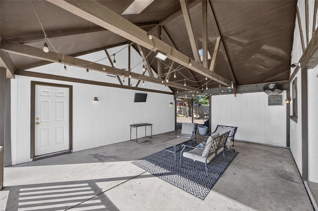 Covered patio featuring an exposed-beam vaulted ceiling, concrete flooring, exterior-grade wall paneling, and string lighting