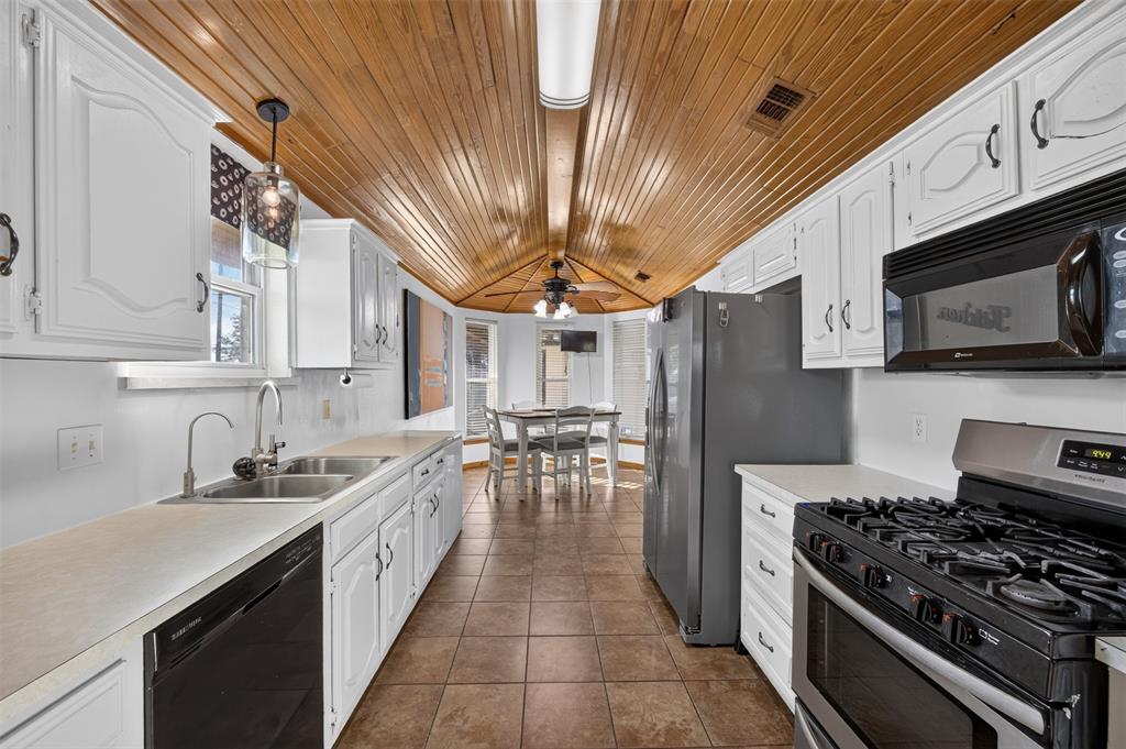 Kitchen featuring vaulted wood-plank ceilings, white cabinetry, tile flooring, stainless steel appliances, and a double-basin stainless steel sink