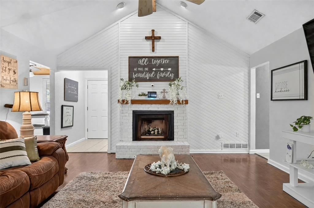 Vaulted ceilings, painted brick fireplace with a wood mantel, diagonal shiplap accent wall, and wood-finish flooring