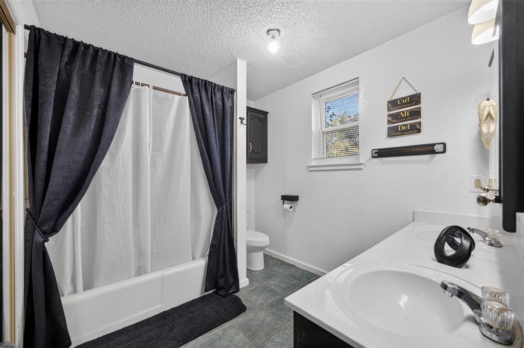 Dual-sink vanity with integrated countertop, tiled flooring, bathtub and shower combination, wall-mounted cabinetry, and window