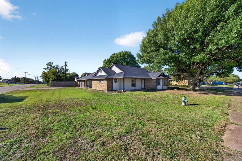 Single-story brick and siding exterior featuring an asphalt shingle roof, bay window, and expansive lawn with mature shade trees