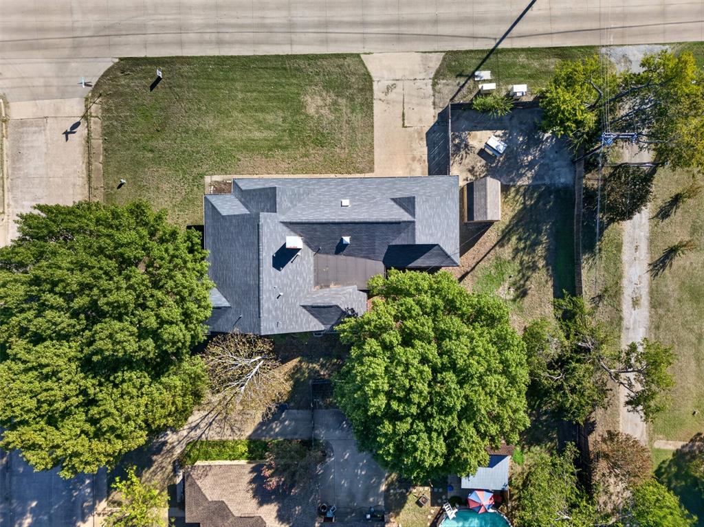 Aerial perspective featuring a multi-gabled asphalt shingle roof, mature canopy trees, concrete driveway, and a detached storage structure on a rectangular lot