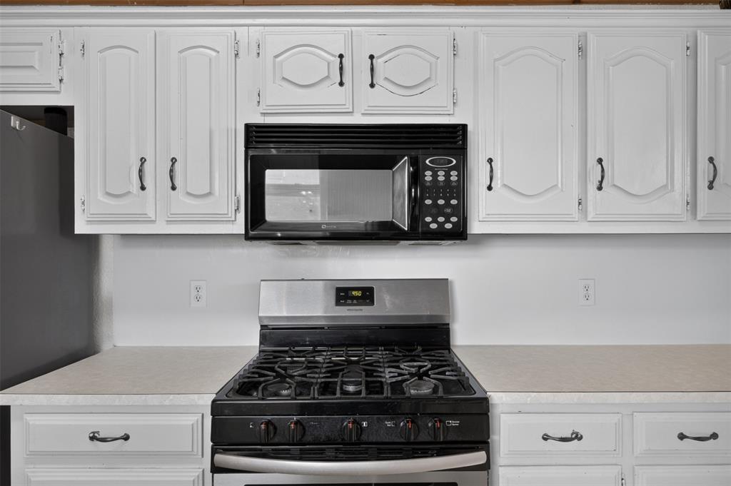 White cabinetry with traditional panel detailing, built-in over-the-range microwave, stainless steel gas range, and expansive solid-surface countertops