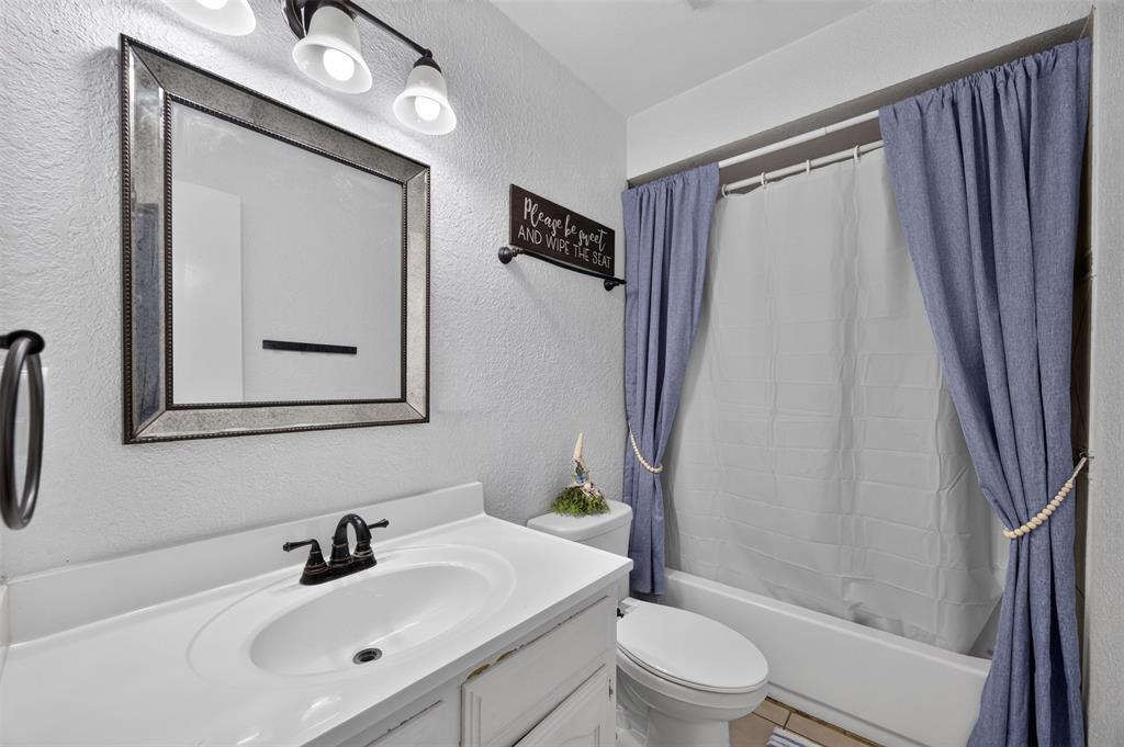 Bathroom featuring a white vanity with an integrated basin, matte black faucet, framed mirror, three-light vanity fixture, and a bathtub-shower combination