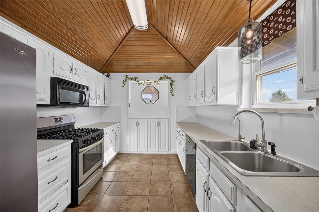 Kitchen featuring white cabinetry, vaulted wood-paneled ceiling, stainless steel gas range, tiled flooring, and dual-basin stainless steel sink with high-arch faucet